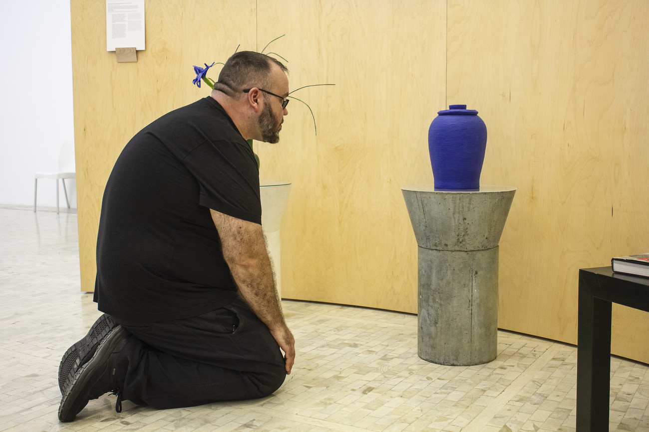 Steve Giasson. Performance invisible n&deg; 160 (S'agenouiller devant une &oelig;uvre d'art). Eduardo Costa. Monumento conmemorativo para Scott Burton. (Monument comm&eacute;moratif de Scott Burton). S.d. Trois peintures acryliques volum&eacute;triques de lys avec vase. Urne fun&eacute;raire en peinture acrylique volum&eacute;trique et cendres de Scott Burton. 1999-2000. Imitation de la Table de Scott Burton, acrylique volum&eacute;trique et poussi&egrave;res de marbre. 1995-97. Table de Scott Burton, b&eacute;ton arm&eacute;. 1980. Table en bois Thompson. 1991-2003. Catalogue d'exposition de Scott Burton, Instituto Valencia de Arte Moderno. 2004. Performeur : Steve Giasson. Cr&eacute;dit photographique : Martin Vinette. Museo Tamayo, Ciudad de M&eacute;xico. 2 novembre 2017.